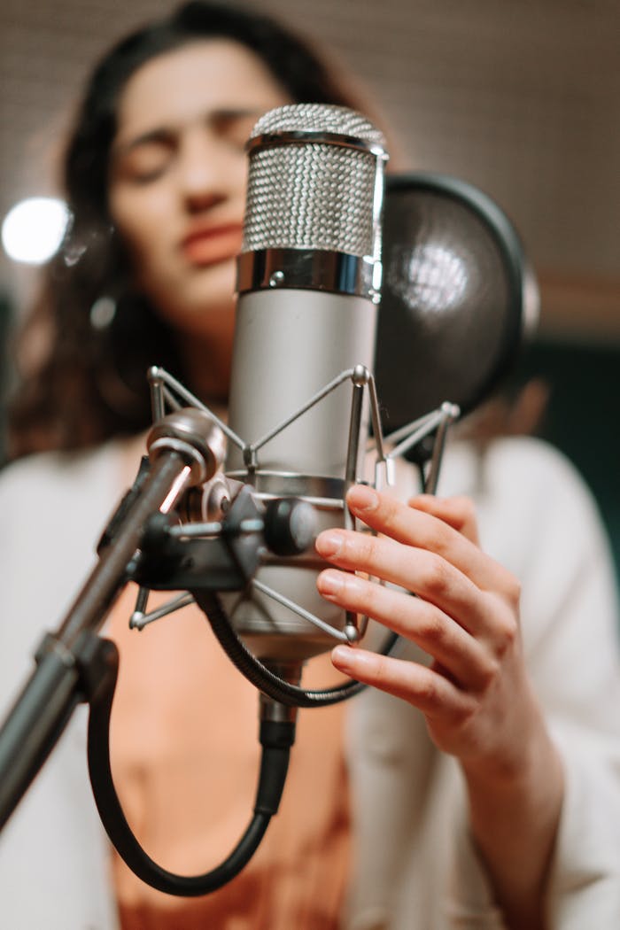 A woman singing passionately into a condenser microphone in a modern music studio.